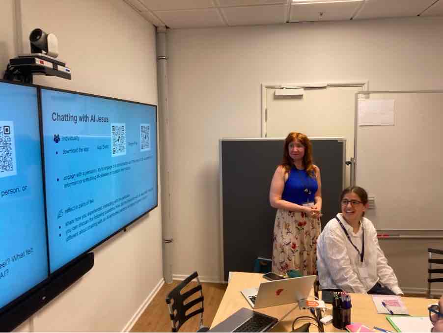 Session auf der DASTS-Konferenz: Folie „Chatting with AI Jesus“ auf dem Bildschirm, daneben eine Vortragende; im Vordergrund eine Teilnehmerin am Tisch.